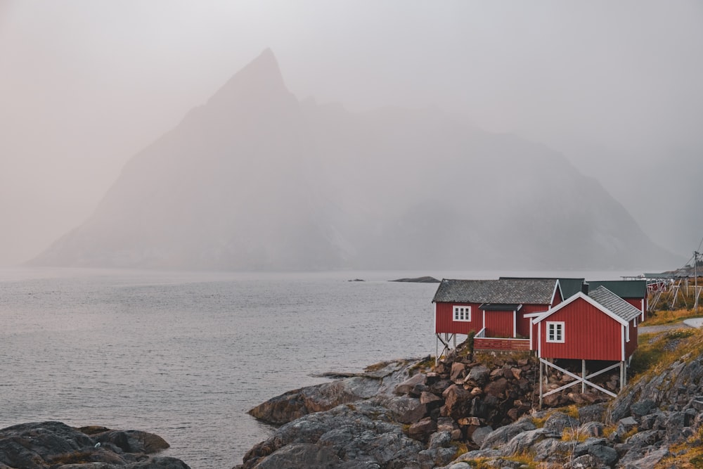 a red house sitting on top of a rocky hill next to a body of water