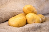 A group of potatoes resting on a textured burlap surface, highlighting their smooth, clean skins and light brown color.