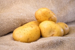 A group of potatoes resting on a textured burlap surface, highlighting their smooth, clean skins and light brown color.