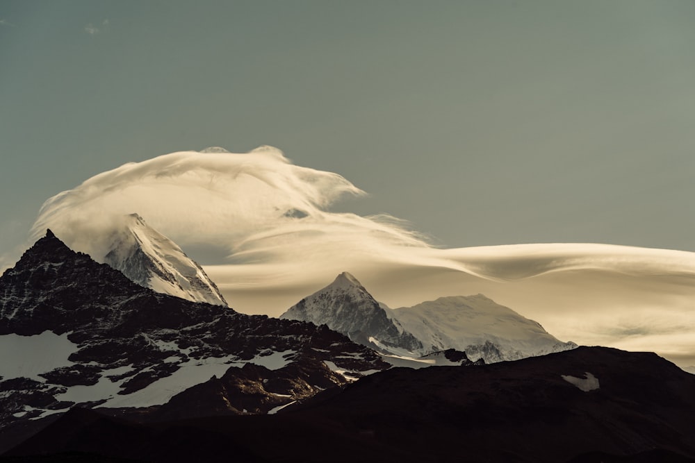 a mountain covered in clouds and snow under a blue sky