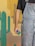 A person wearing paint-splattered denim overalls holds a green paintbrush. The background includes a painted desert scene featuring stylized cacti and a canyon with colors ranging from beige to orange.