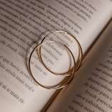 A pair of minimalist gold hoops resting on an open book with natural sunlight.
