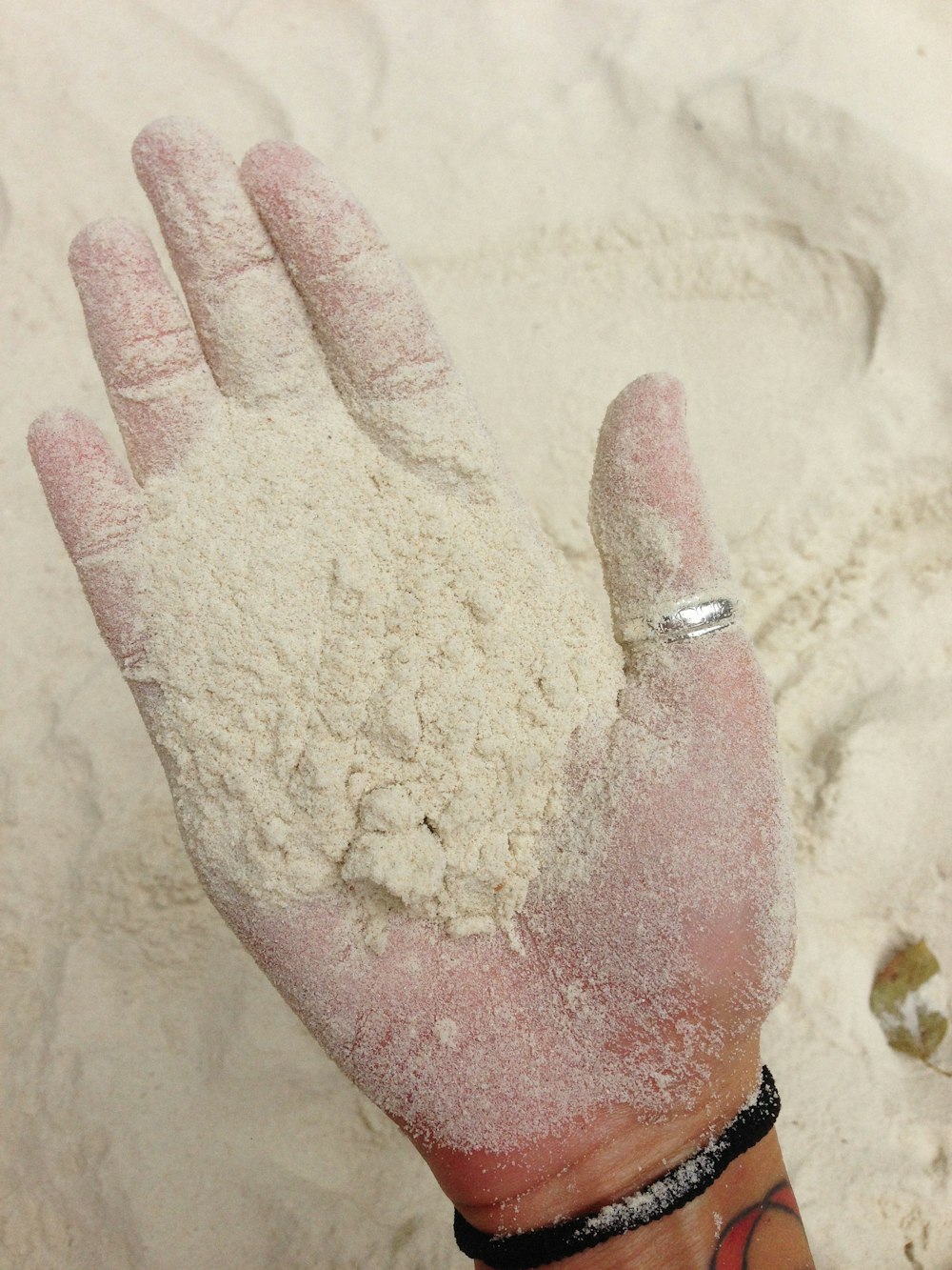 a hand with a ring on it covered in sand