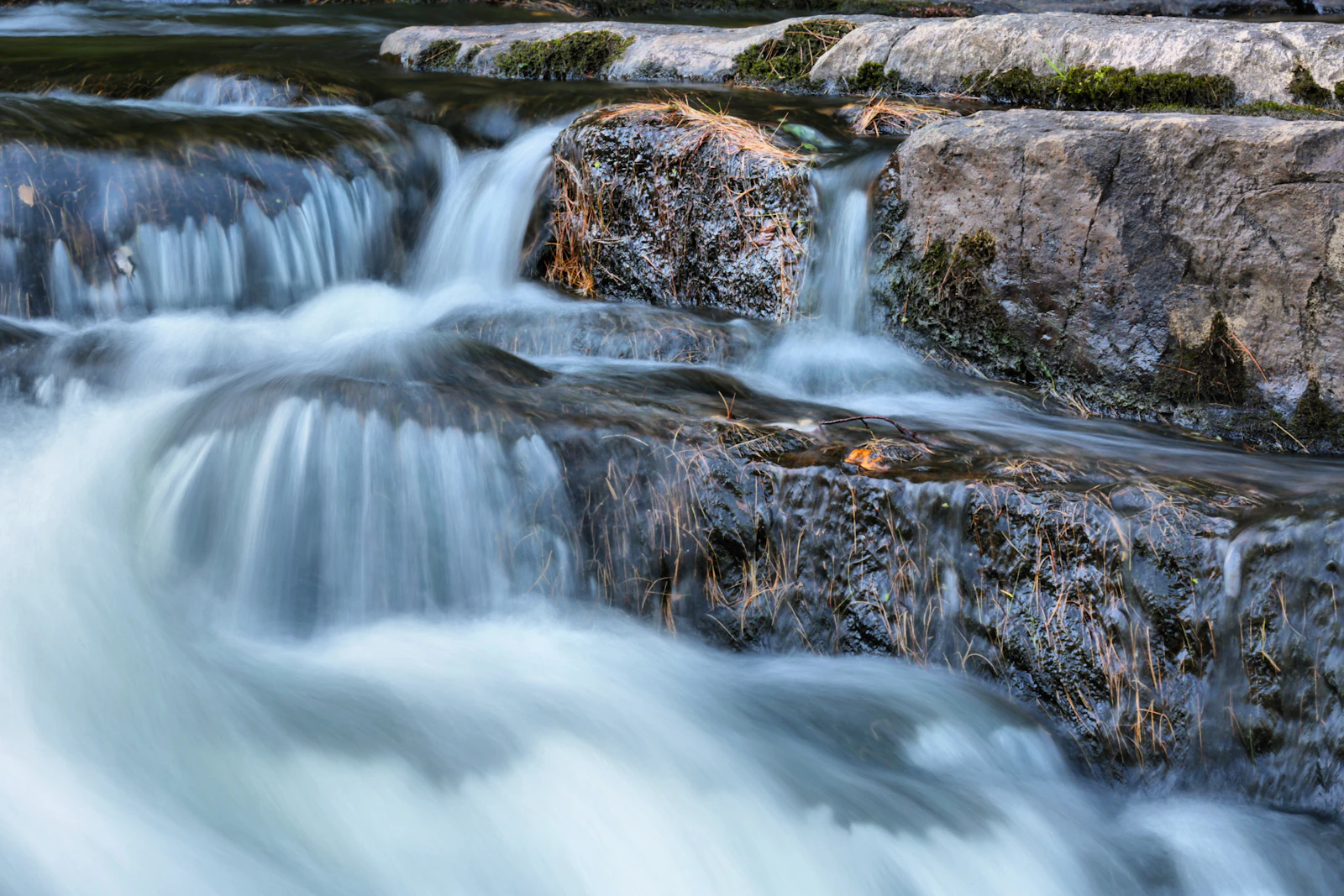 Langzeitbelichtung eines Wasserstroms über Felsen in einen Fluss