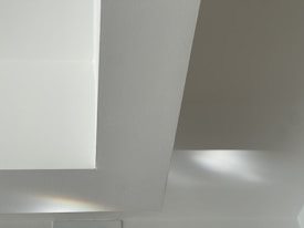 A minimalist architectural detail featuring clean lines and geometric shapes, with soft lighting creating subtle shadows and highlights. The smooth surface appears to be made of a concrete or plaster material.