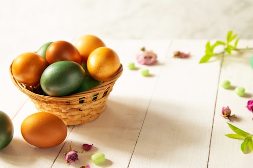 A rustic basket filled with colorful Easter eggs wrapped in shiny foil, surrounded by spring flowers.