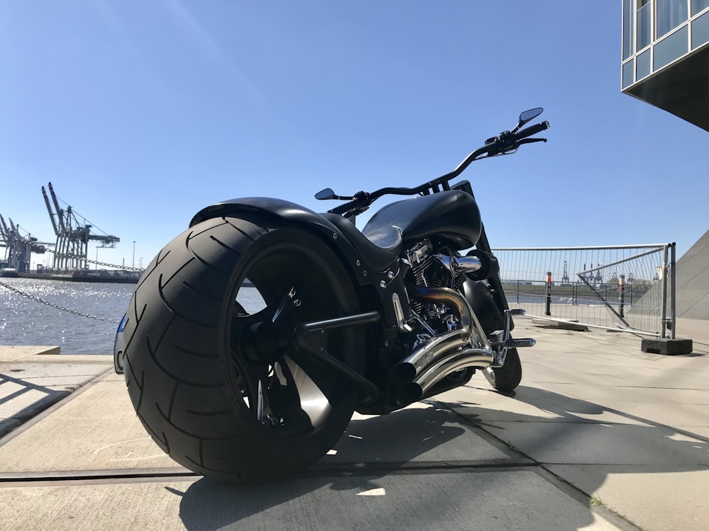 a black motorcycle parked on a sidewalk next to a body of water