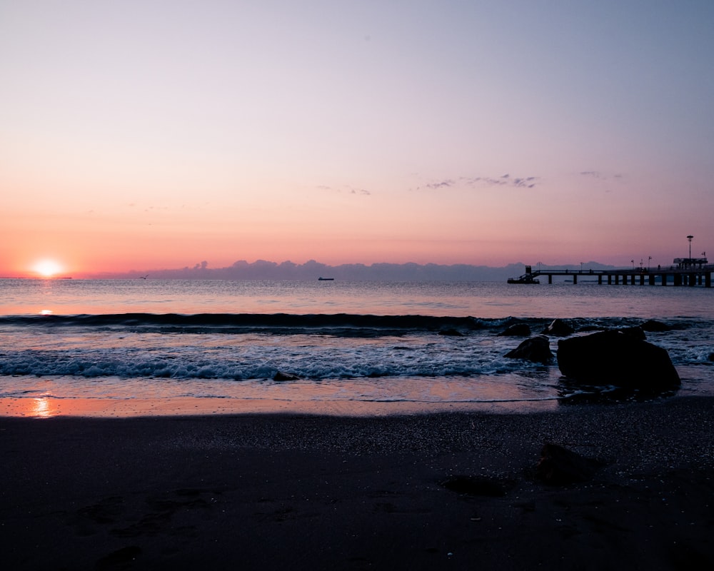 um pôr do sol sobre o oceano com um píer à distância