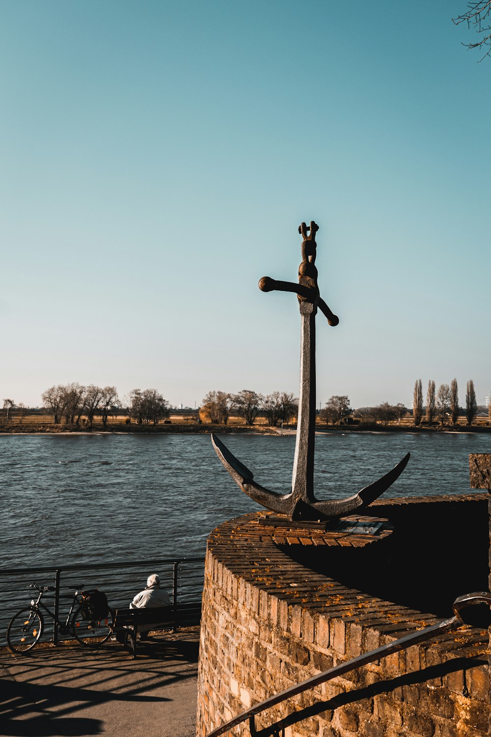 a statue of an anchor on a brick wall next to a body of water