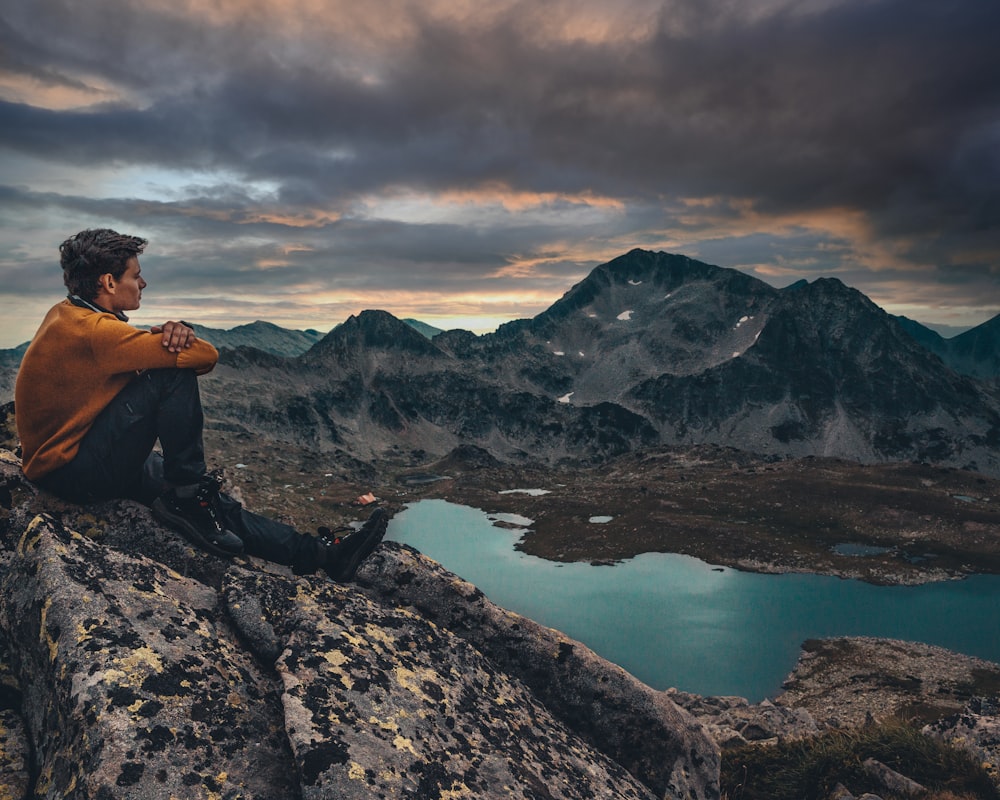 a man sitting on top of a rock next to a lake