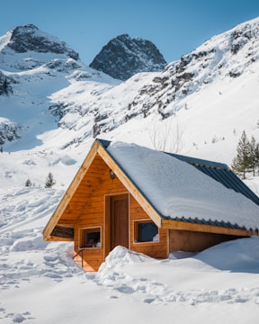 A sleek prefabricated cottage perched on a steep hillside with snow-capped peaks in the background.