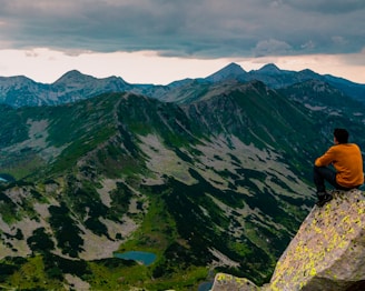 a man sitting on top of a mountain next to a lake