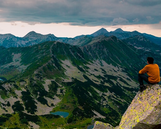 a man sitting on top of a mountain next to a lake