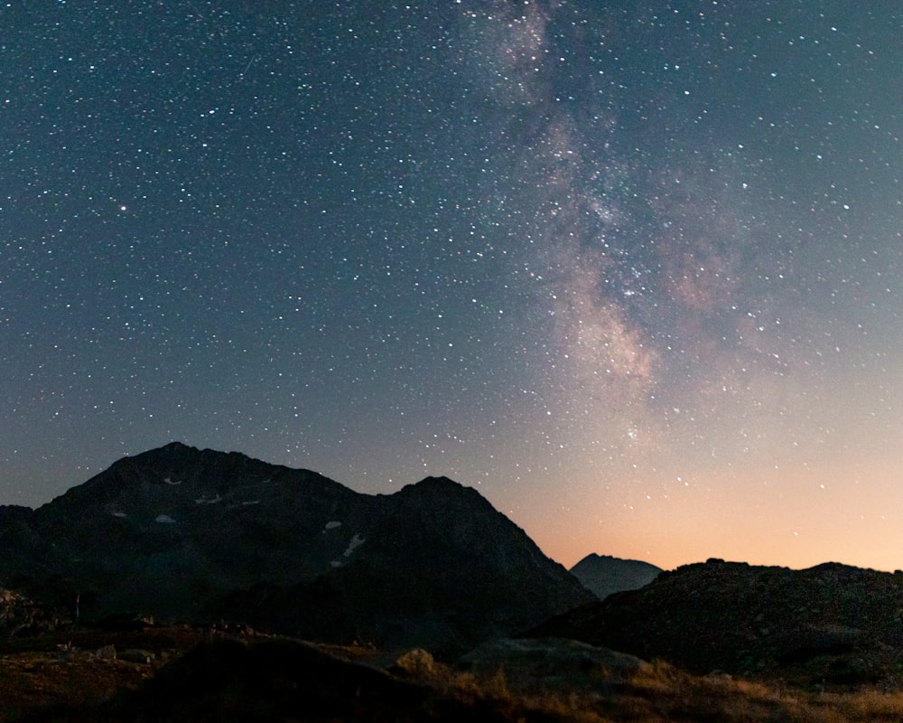 the night sky with stars above a mountain range