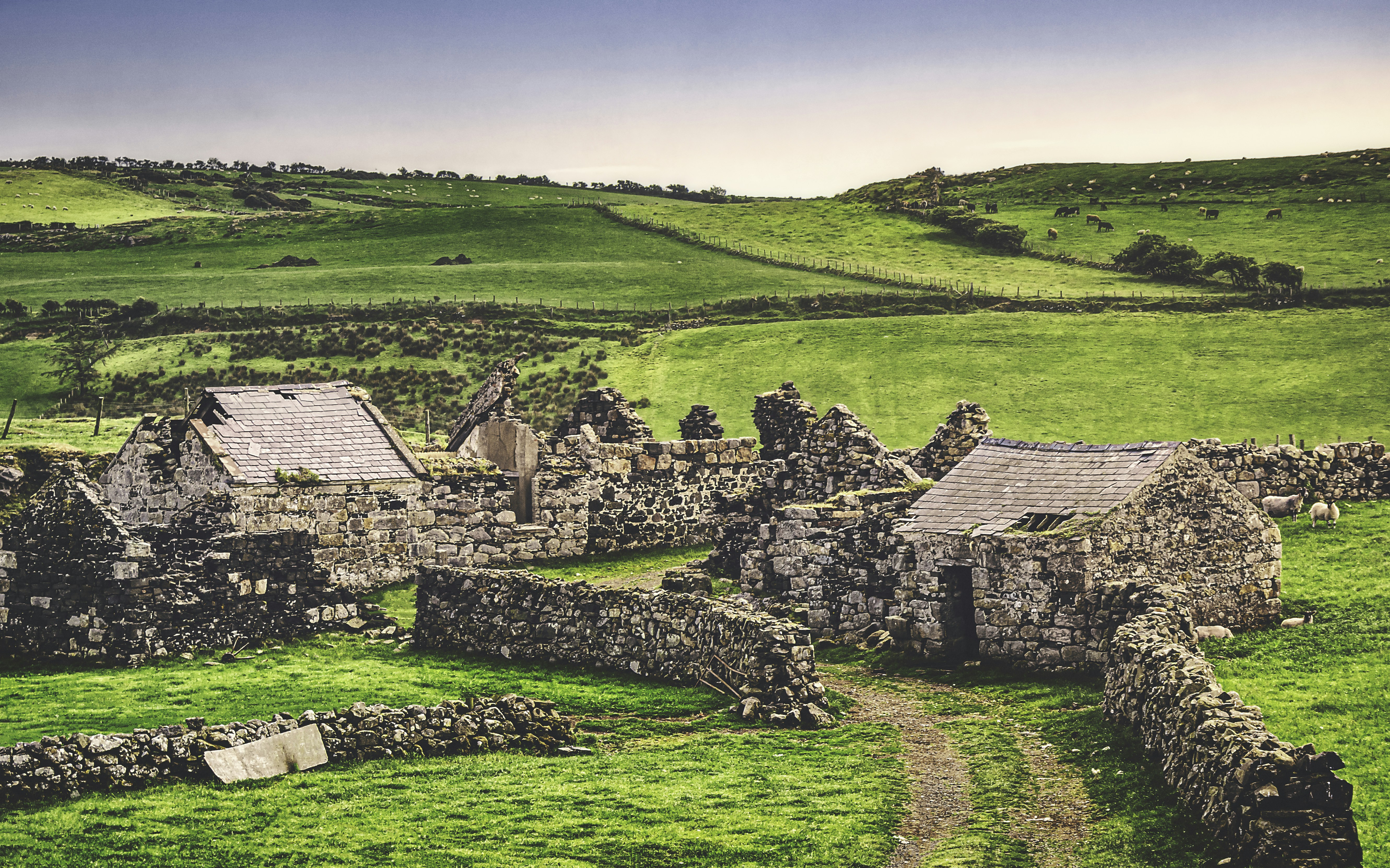 an old stone house in the middle of a green field
