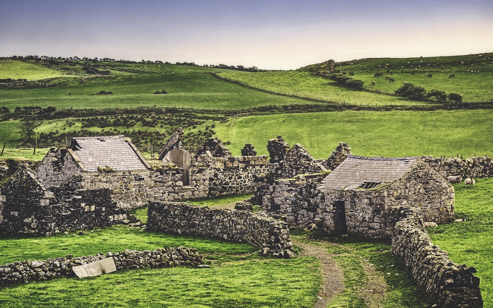 an old stone house in the middle of a green field