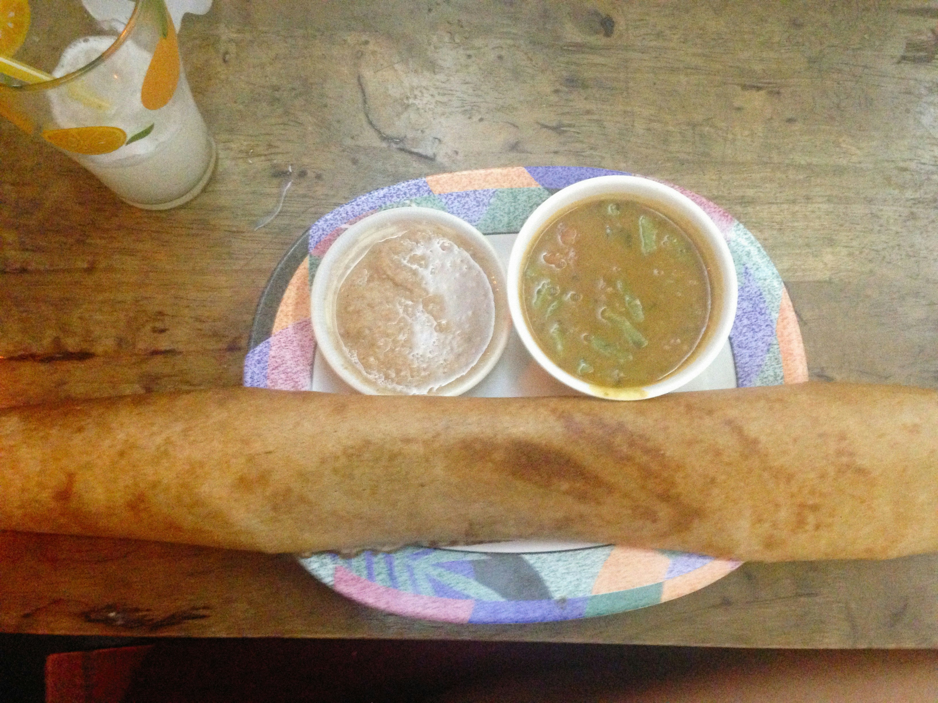 A long rolled dosa in front of two small bowls of dipping sides