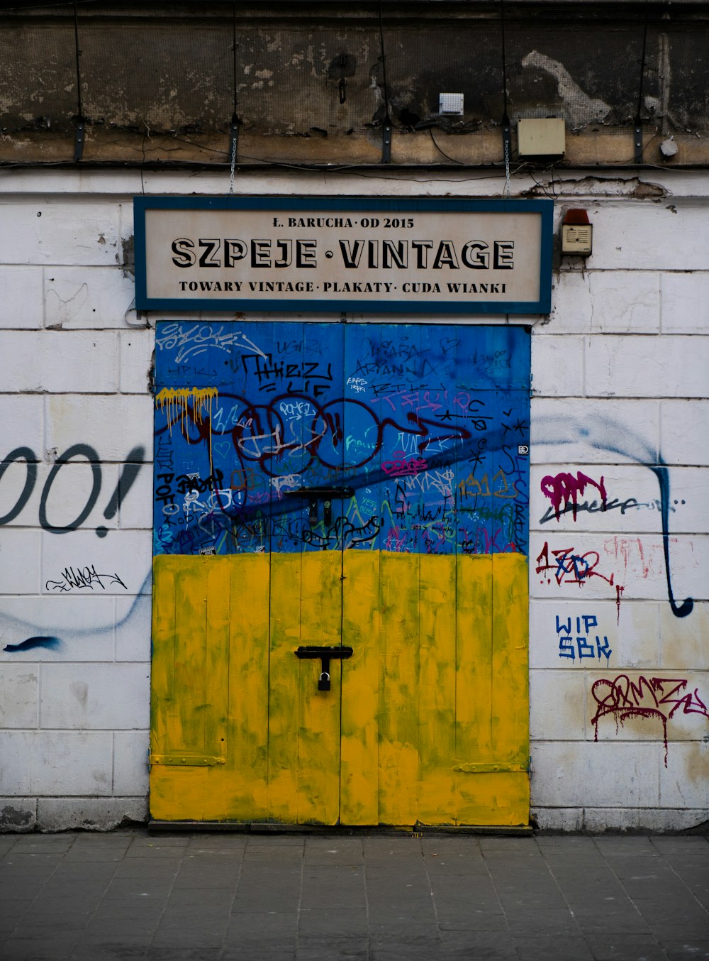 a yellow door with graffiti on it in front of a white brick wall