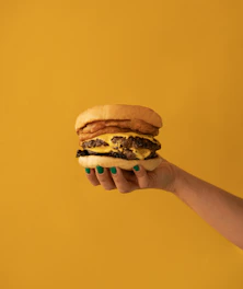 a hand holding a cheeseburger on a yellow background