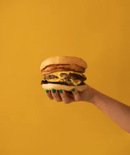 a hand holding a cheeseburger on a yellow background