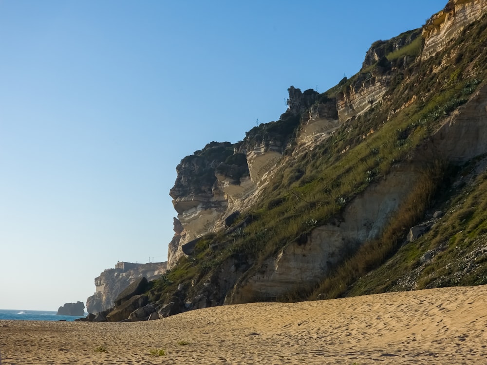 a sandy beach next to a cliff on a sunny day