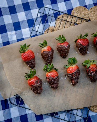 A close-up of strawberries being dipped into melted chocolate in a cozy kitchen setting.