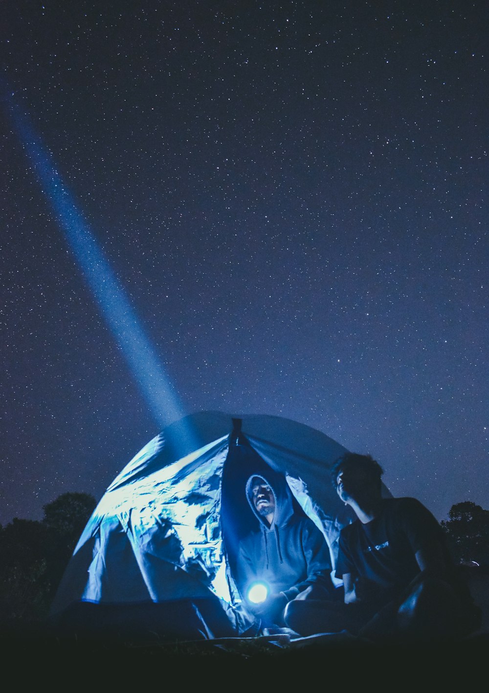a man sitting in front of a tent under a sky filled with stars