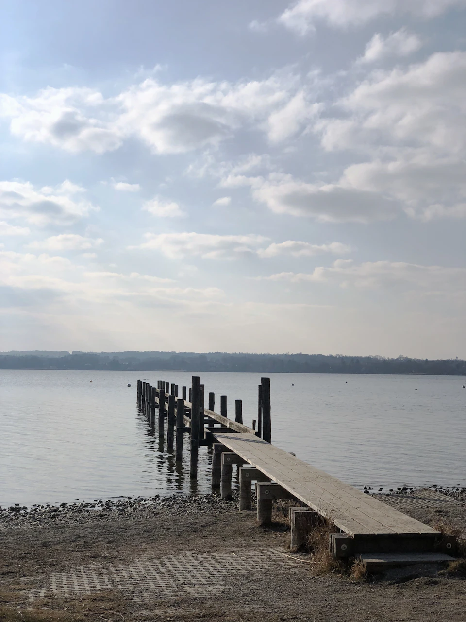 Serene wooden pier extends into calm waters, surrounded by weathered posts and lush greenery