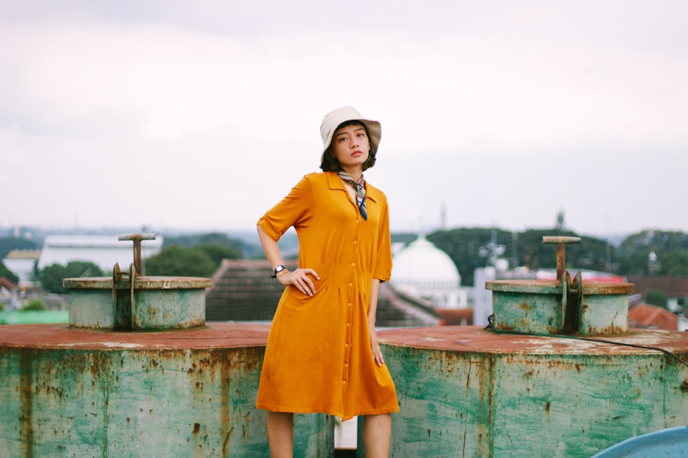 a woman in a yellow dress and hat standing on a roof