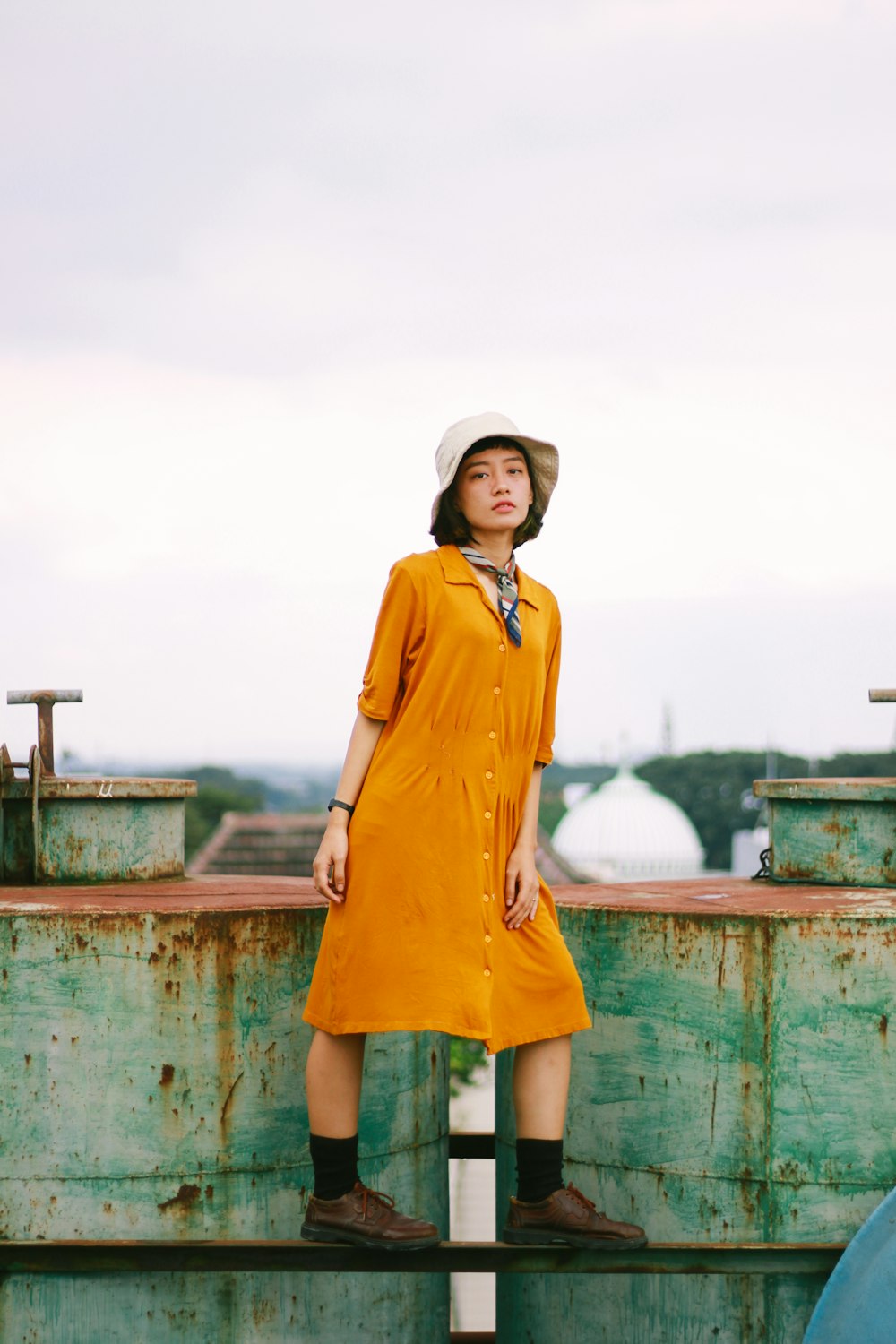 a woman in a yellow dress and hat standing on a rail