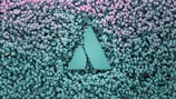 A geometric logo with two triangular shapes is embedded in a backdrop of numerous small spherical objects that transition from teal at the bottom to pink at the top.