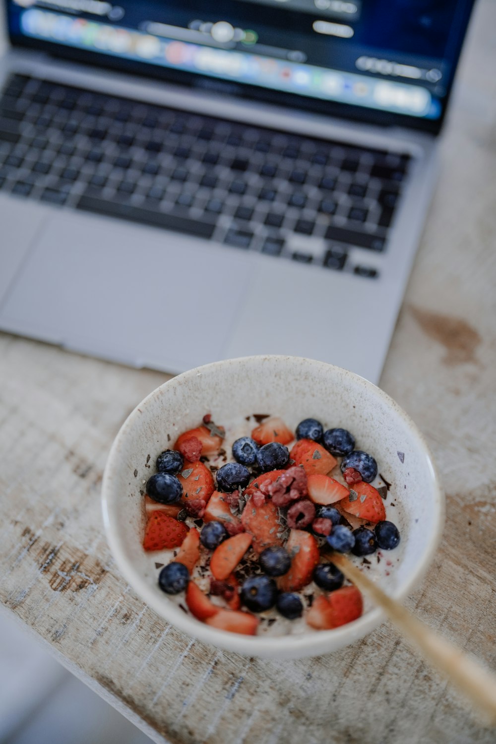 a bowl of strawberries and blueberries in front of a laptop