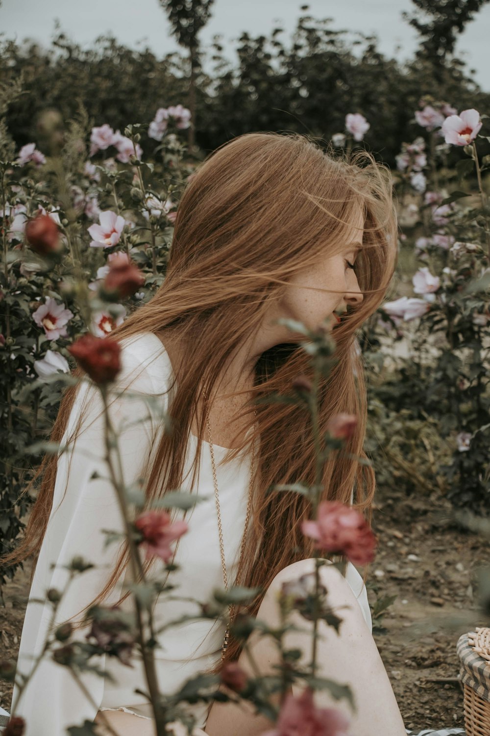 a woman with long red hair sitting in a field of flowers