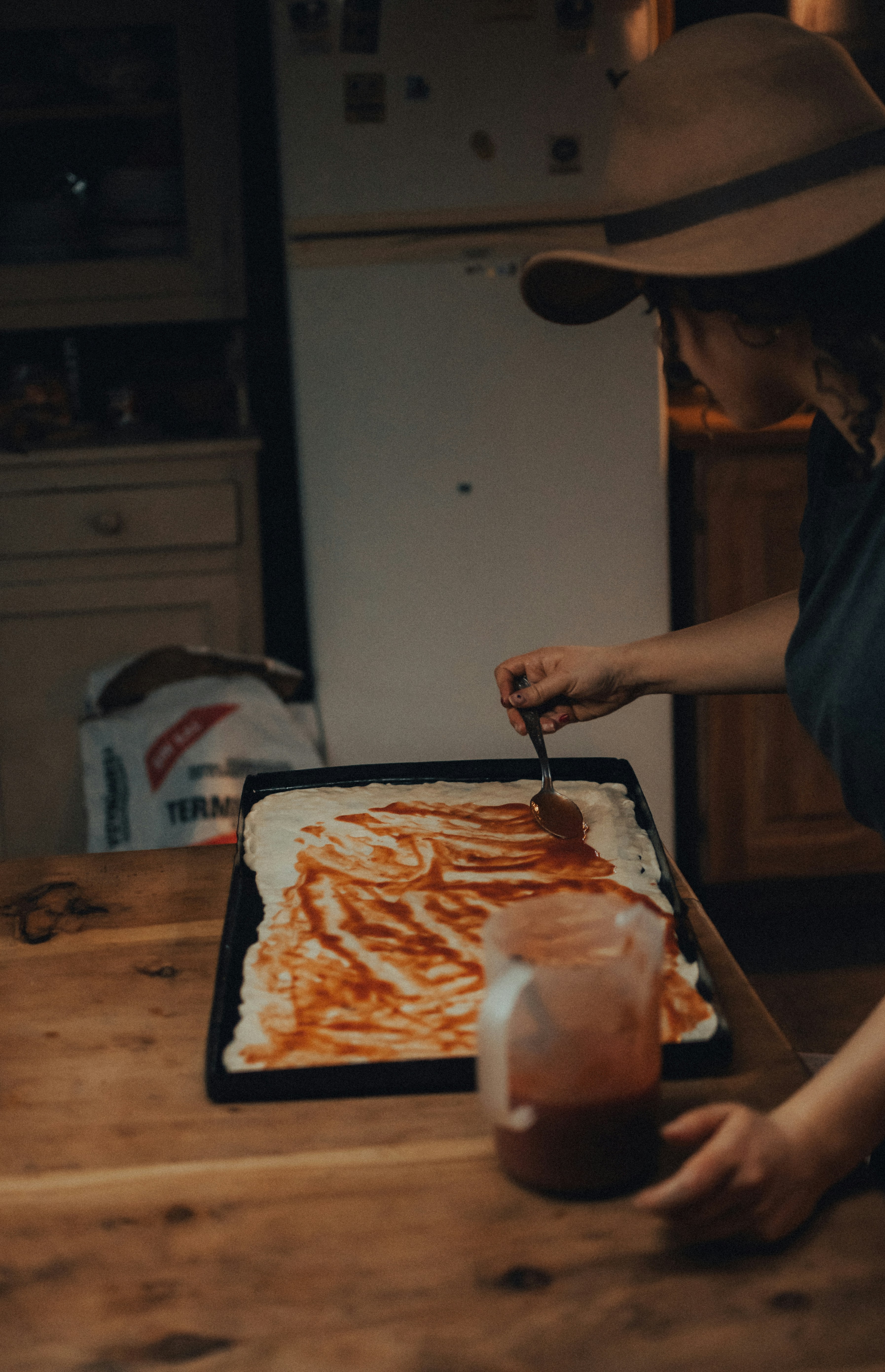 Person in cowboy hat drizzling sauce onto homemade dessert pizza`