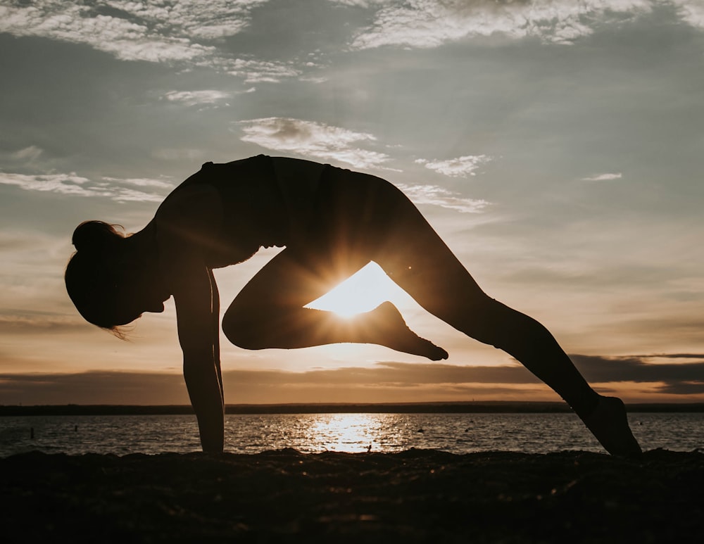 a woman doing a yoga pose in front of the sun