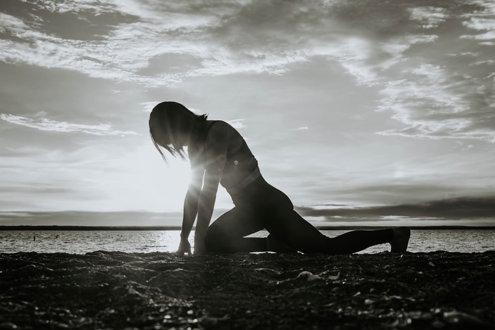 a woman kneeling down on the ground in front of a body of water