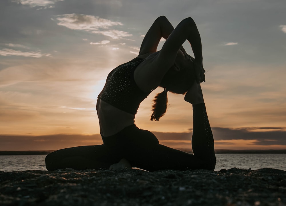 a woman doing yoga on the beach at sunset