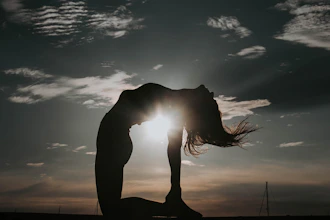 a woman doing a yoga pose in front of the sun
