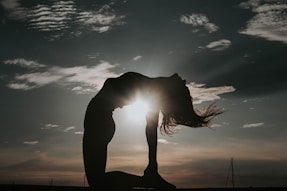 a woman doing a yoga pose in front of the sun