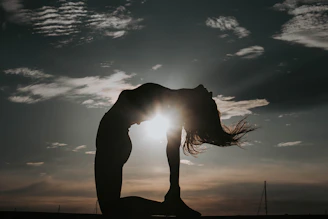 a woman doing a yoga pose in front of the sun
