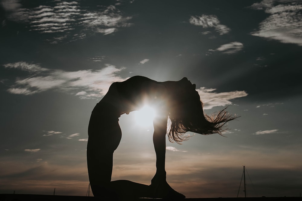 a woman doing a yoga pose in front of the sun