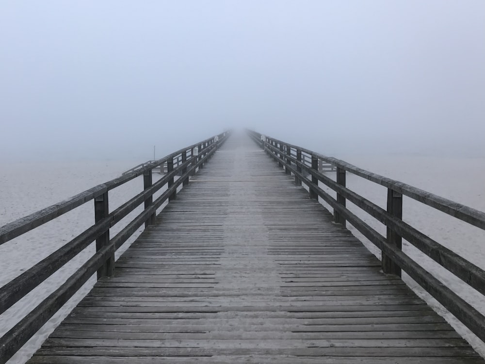 a long wooden pier extending into the ocean on a foggy day