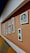 A series of framed pictures are arranged on a peach-colored wall. The frames vary in size and shape, displaying both photographs and artwork. One prominent picture features a person holding a camera. The setting includes a cushioned seating area with shades of brown and yellow.