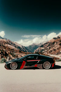 A sleek black luxury sports car parked on a scenic Swiss mountain road at sunset.