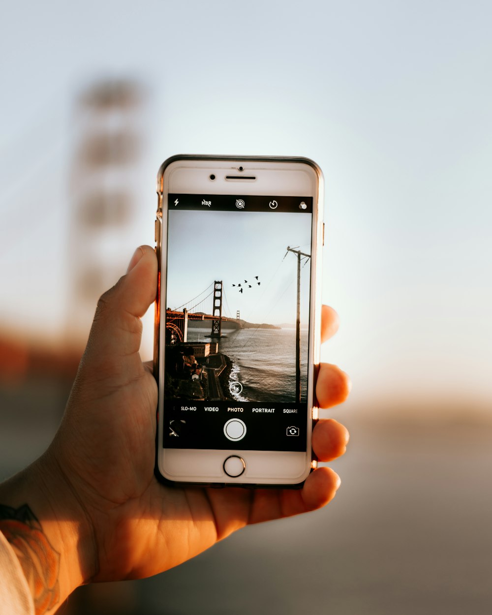 uma pessoa segurando um telefone celular para tirar uma foto da ponte do portão dourado