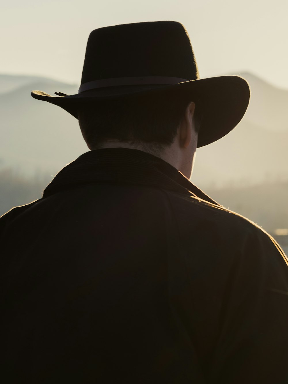 a man in a cowboy hat looking at the mountains