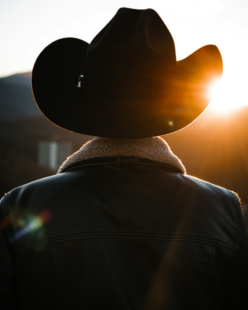 a person wearing a cowboy hat with the sun behind them