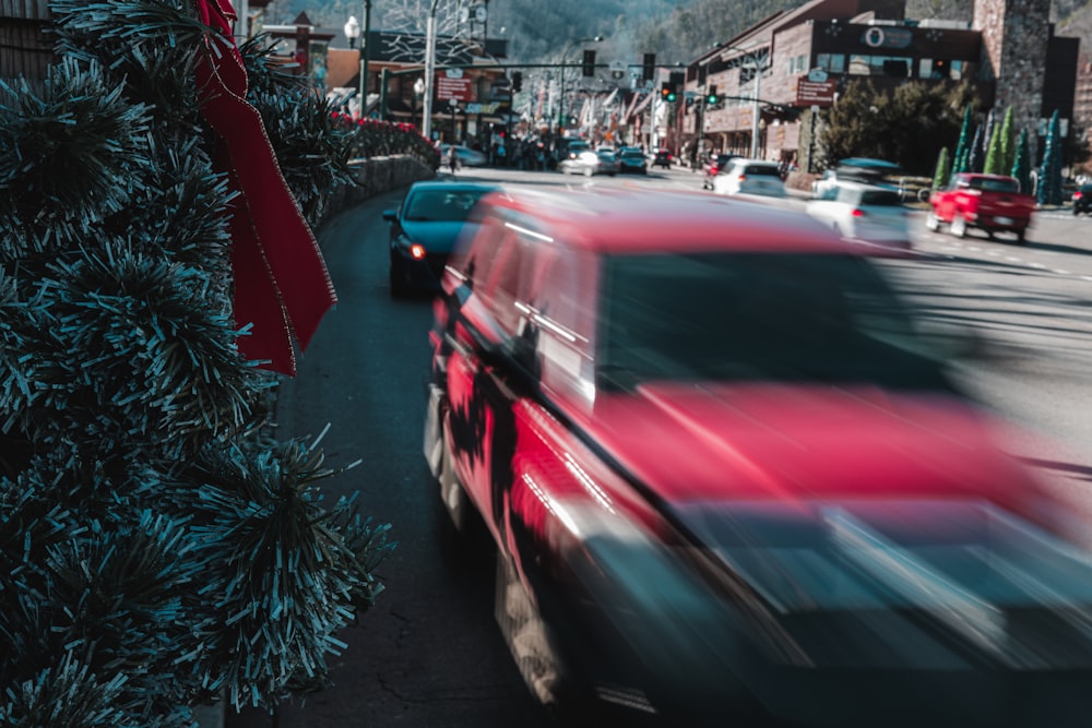 a red car driving down a street next to a christmas tree