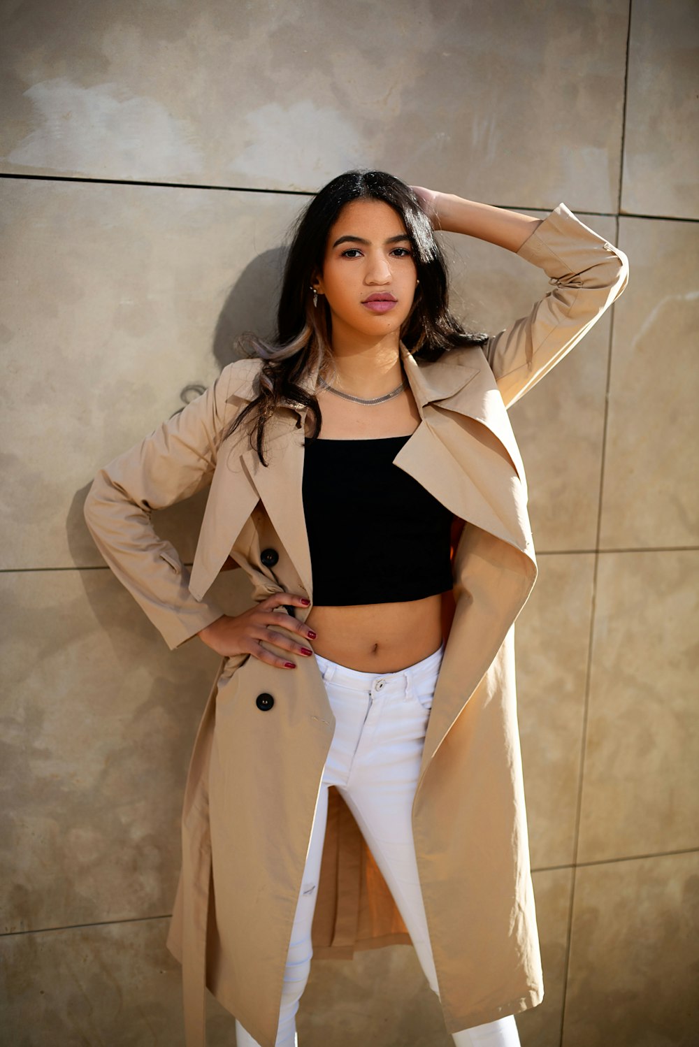 a woman in a trench coat leaning against a wall