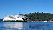 A ferry boat cutting through deep blue waters with Isle Royale’s forested coast in the background.